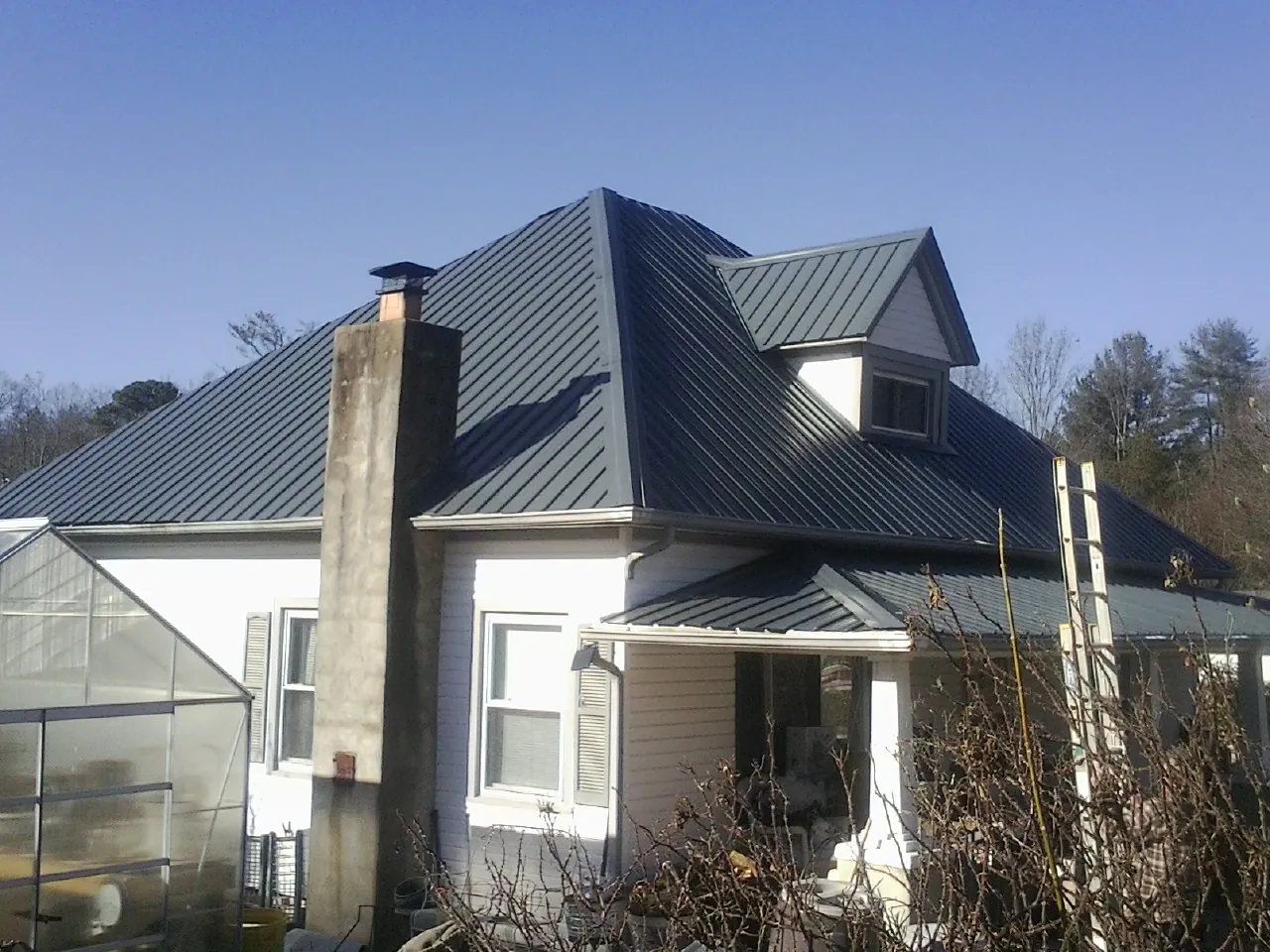 Dark blue standing seam metal roof on a white farmhouse with dormer — Slate & Tile Roof Repair by Roofing Brothers in Deposit