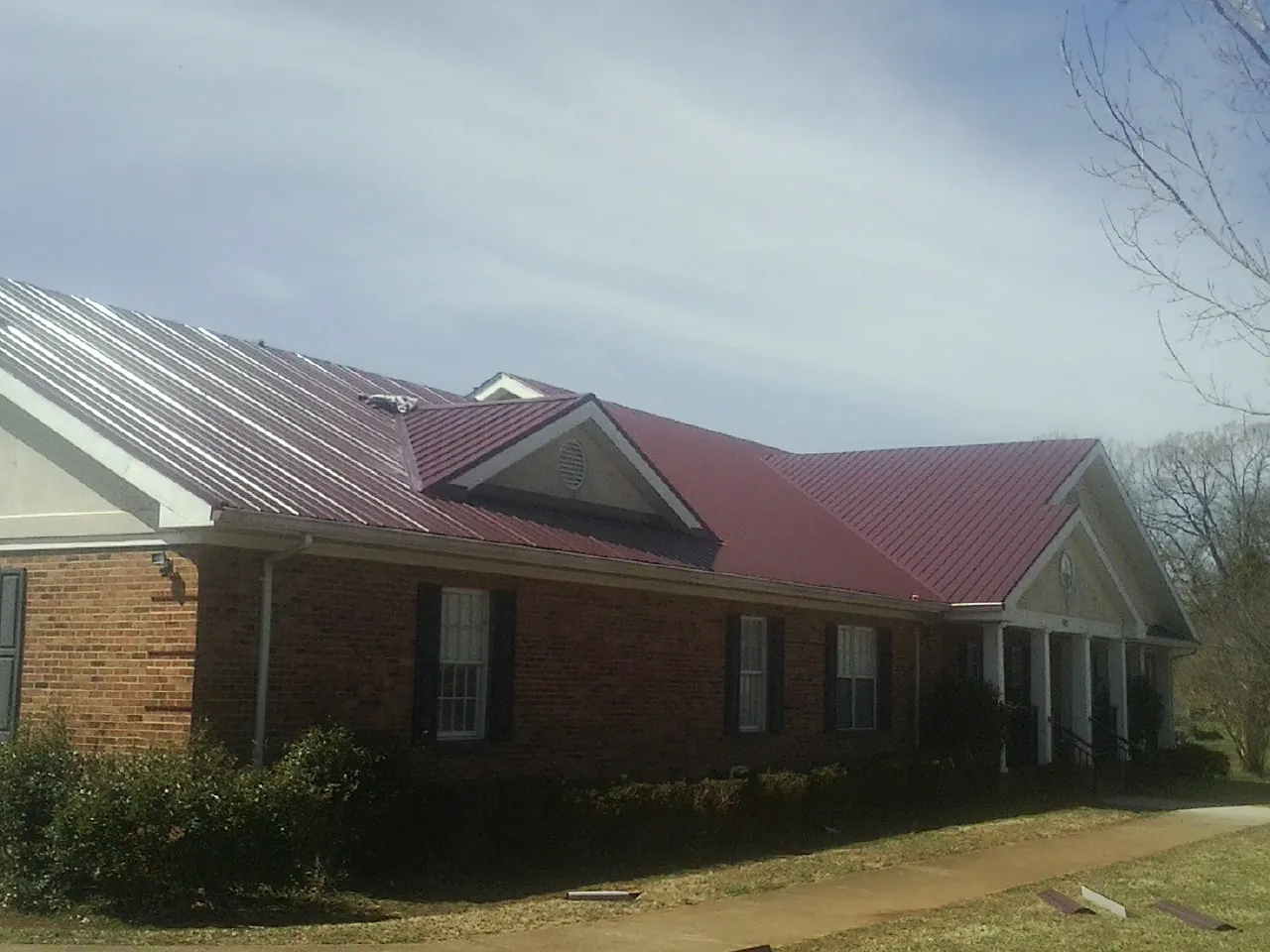Red metal roof with gabled entries on a long brick building, from a Hail Damage Roof Repair job in Deposit