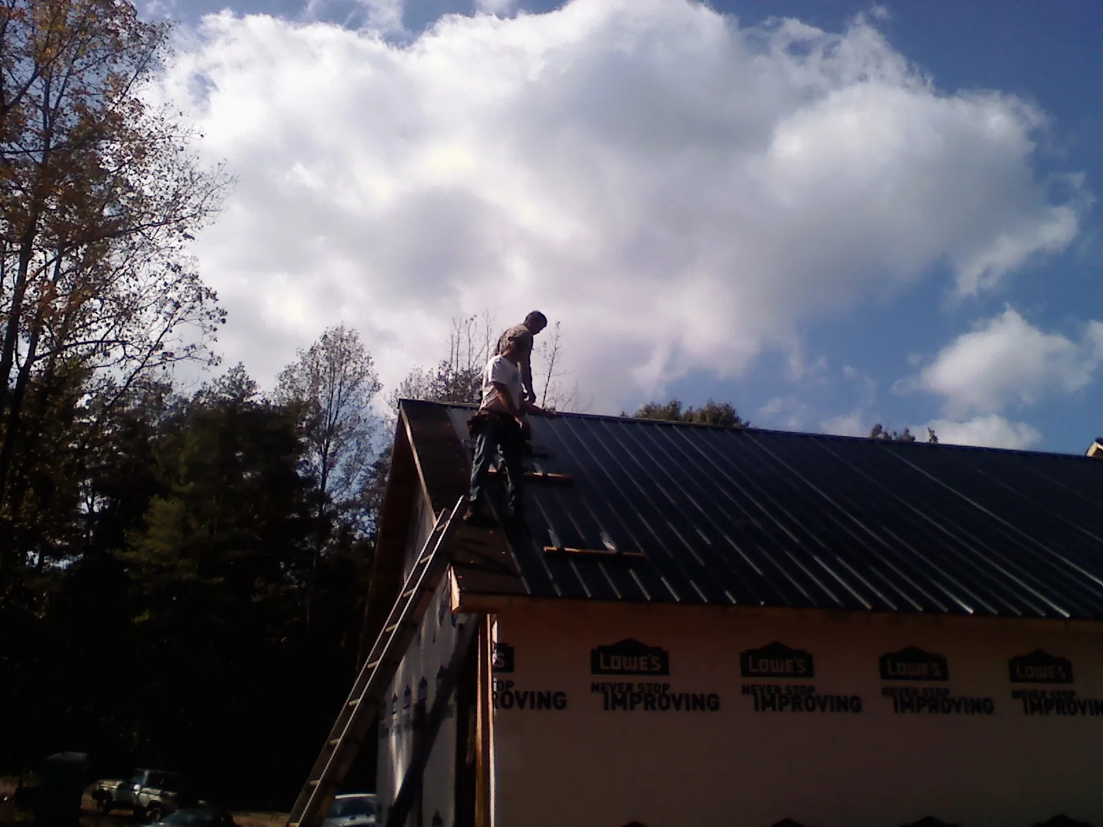 Roofer fastening dark metal panels high against a cloudy sky, from a Roof Inspection job in Deposit