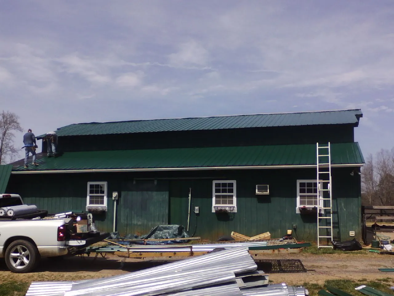Crew installing green metal roofing on a large green barn in Deposit